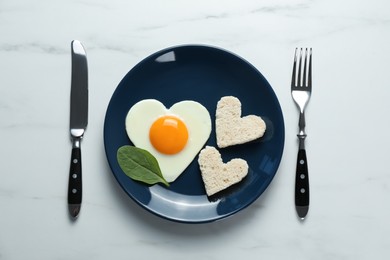 Photo of Romantic breakfast with heart shaped fried egg served on white marble table, flat lay