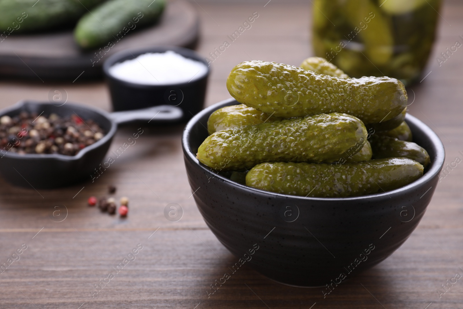 Photo of Bowl of pickled cucumbers and ingredients on wooden table, closeup