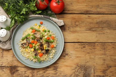 Photo of Delicious bulgur with vegetables and mushrooms served on wooden table, top view. Space for text