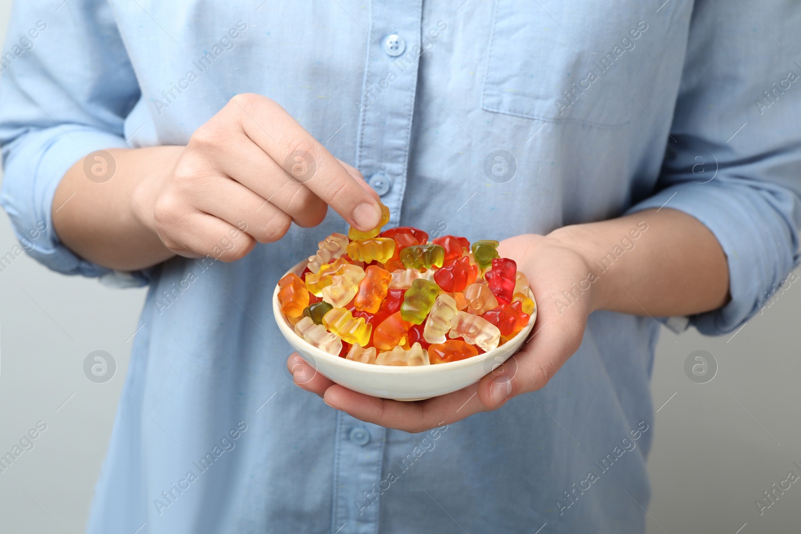 Photo of Woman holding bowl of colorful jelly bears on light background, closeup