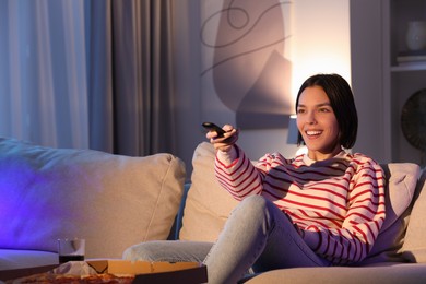 Photo of Happy woman watching TV with pizza on sofa at home, space for text