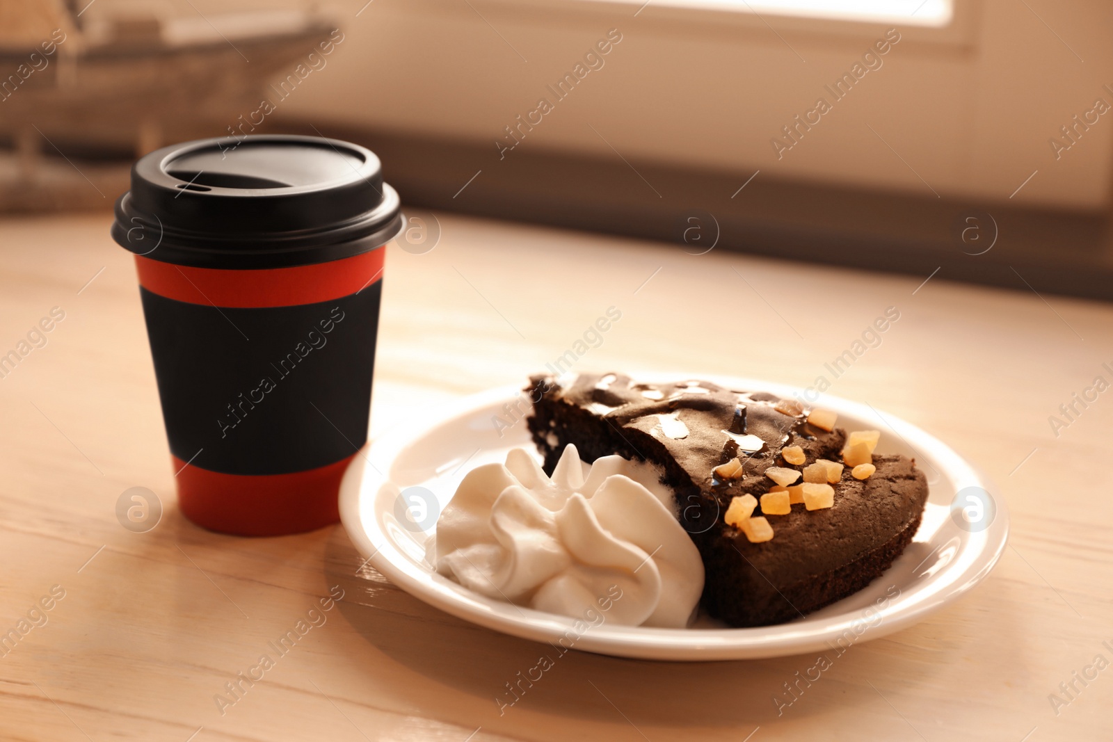 Photo of Tasty coffee in takeaway paper cup and dessert on wooden table indoors