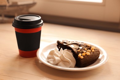 Photo of Tasty coffee in takeaway paper cup and dessert on wooden table indoors