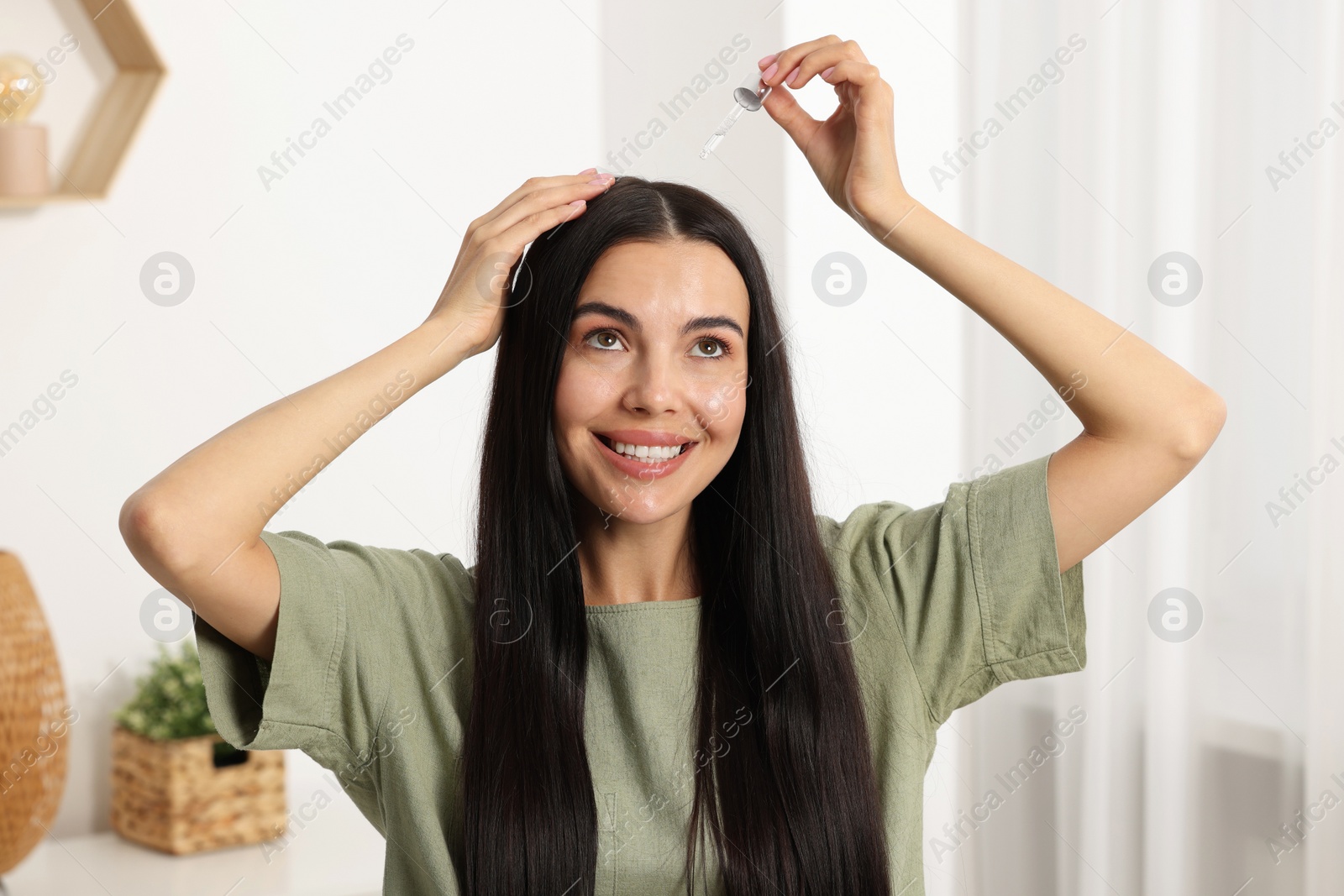 Photo of Beautiful woman applying hair serum in room. Cosmetic product