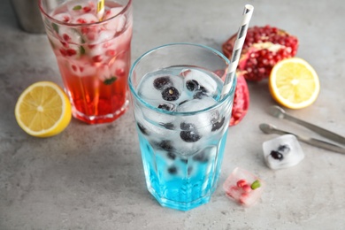 Tasty cocktails with fruit ice cubes on grey table