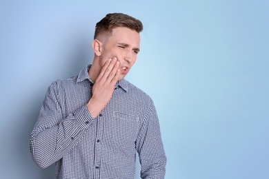 Young man with sensitive teeth on color background