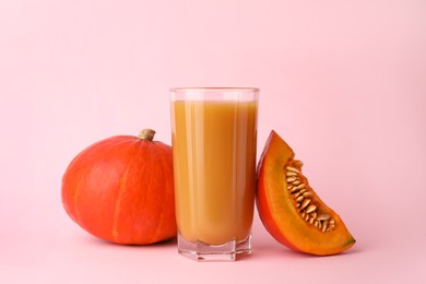 Photo of Tasty pumpkin juice in glass, whole and cut pumpkins on pale pink background