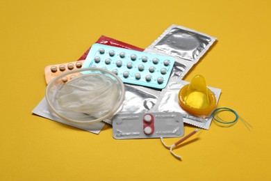Photo of Contraceptive pills, condoms and intrauterine device on yellow background. Different birth control methods