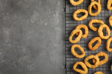 Photo of Cooling rack with fried onion rings on grey table, top view. Space for text