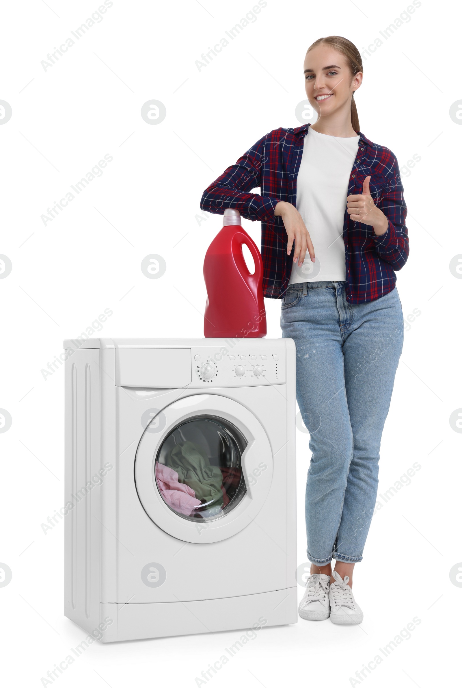 Photo of Beautiful young woman with detergent showing thumbs up near washing machine on white background