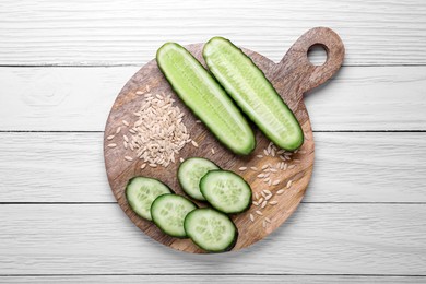 Photo of Pile of vegetable seeds and fresh cucumbers on white wooden table, top view