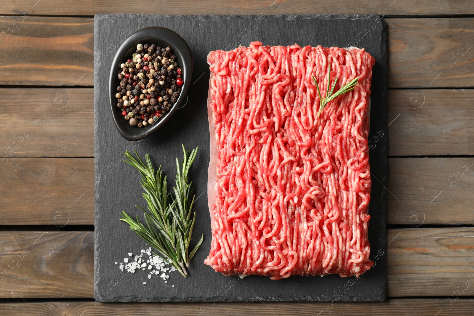 Photo of Raw ground meat, spices and rosemary on wooden table, top view