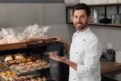 Professional baker near showcase with pastries in store