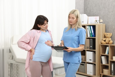 Doctor with clipboard consulting pregnant patient in clinic