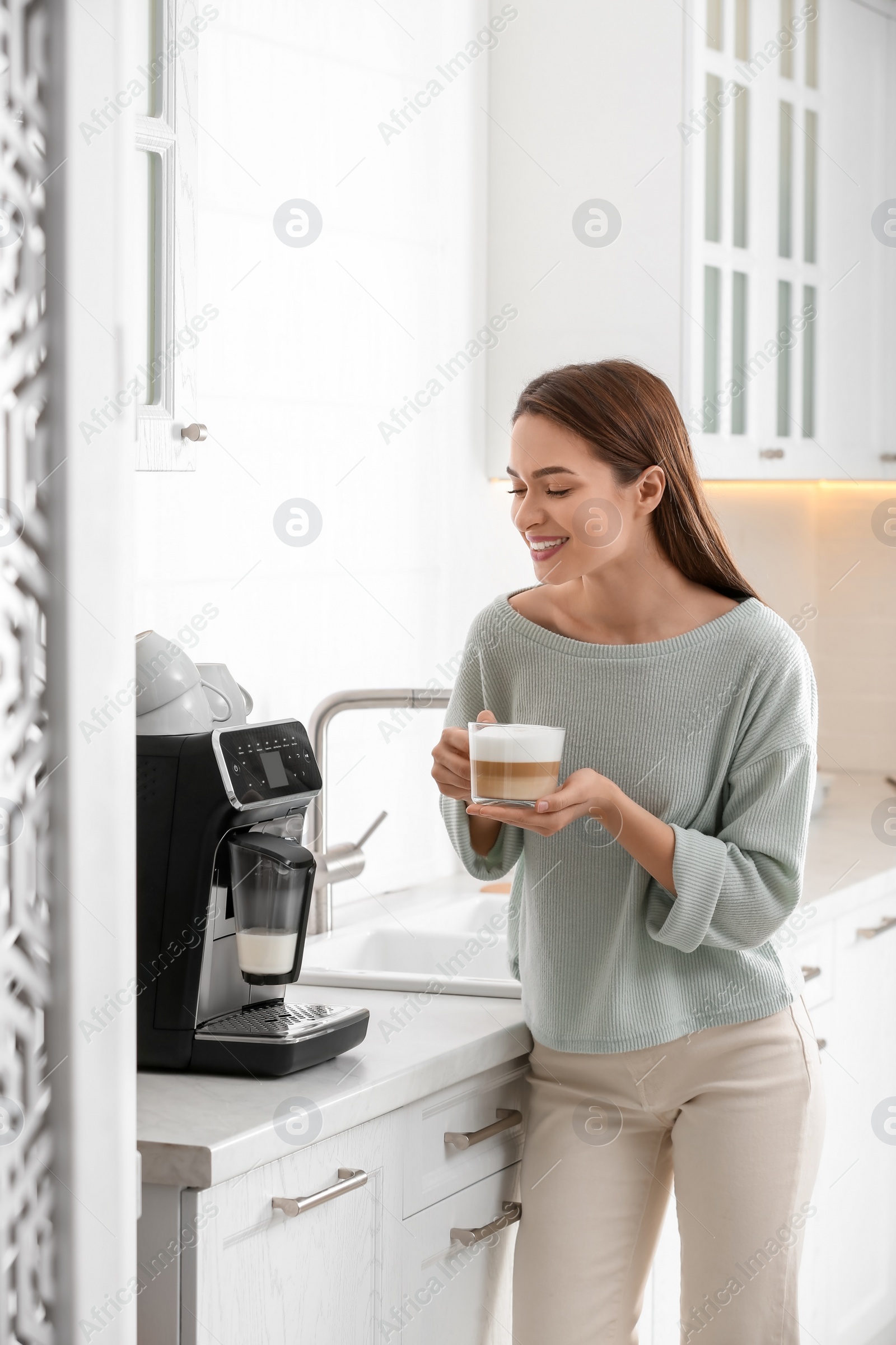 Photo of Young woman enjoying fresh aromatic coffee near modern machine in kitchen