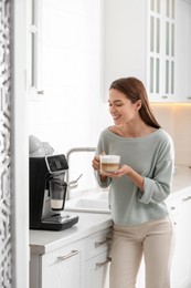 Photo of Young woman enjoying fresh aromatic coffee near modern machine in kitchen