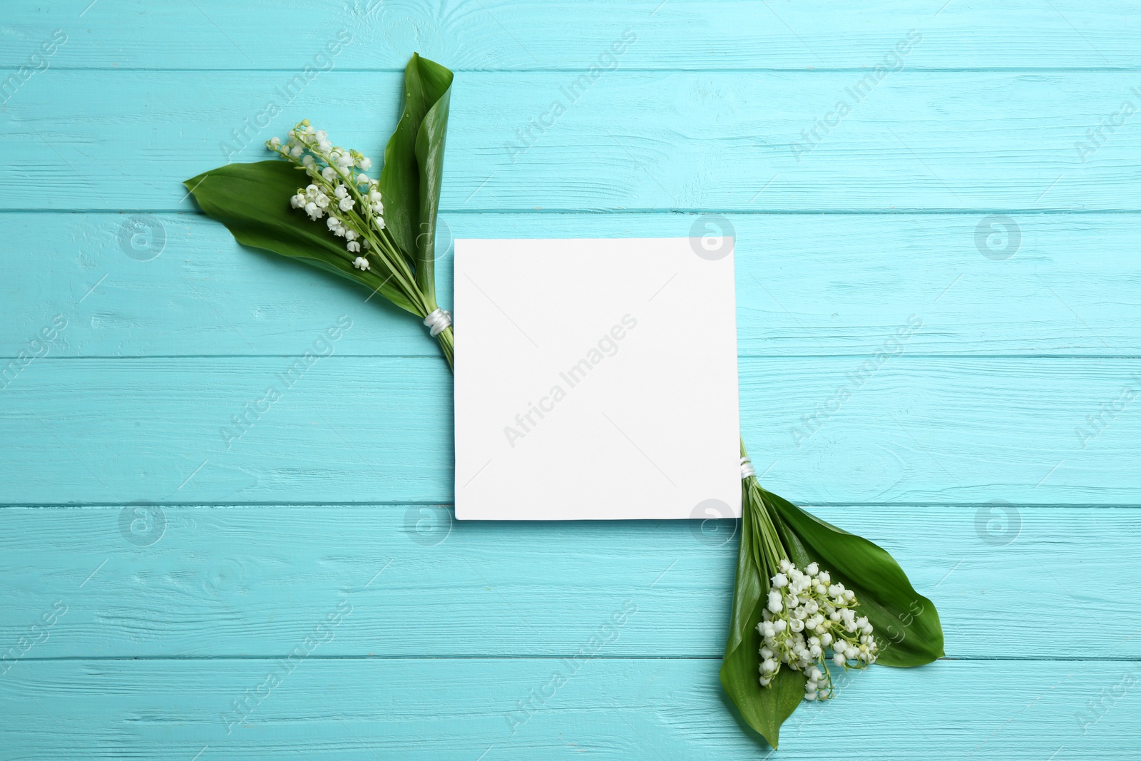 Photo of Blank card with lily of the valley bouquets on wooden background, top view. Space for text