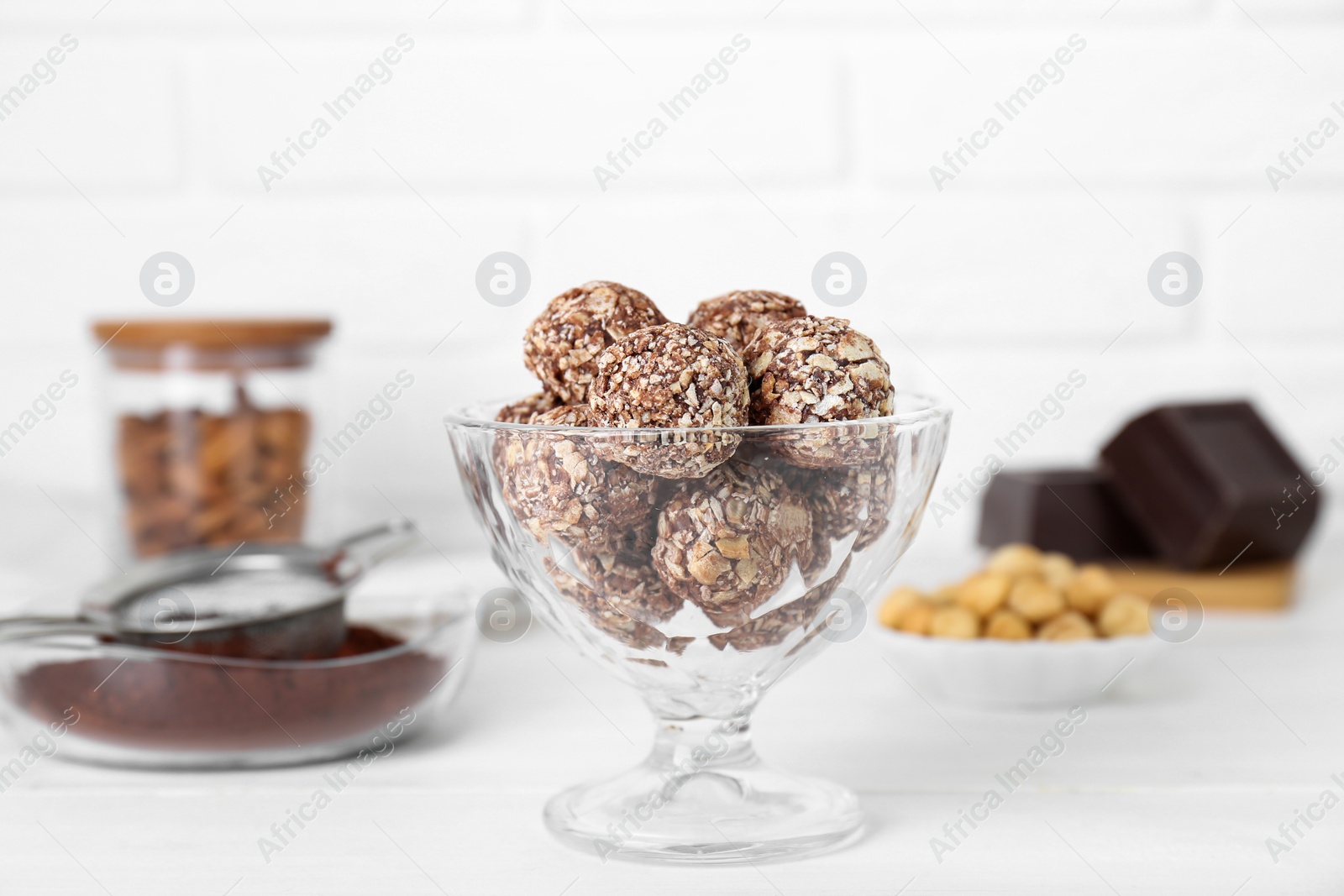 Photo of Glass dessert bowl of tasty chocolate balls on white wooden table, closeup