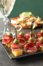 Tasty canapes with olives, prosciutto and cheese on grey table, closeup