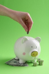 Photo of Financial savings. Woman putting coin into piggy bank on green background, closeup