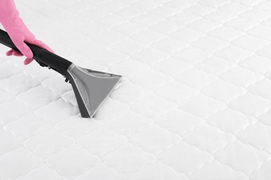 Photo of Person disinfecting mattress with vacuum cleaner, closeup. Space for text