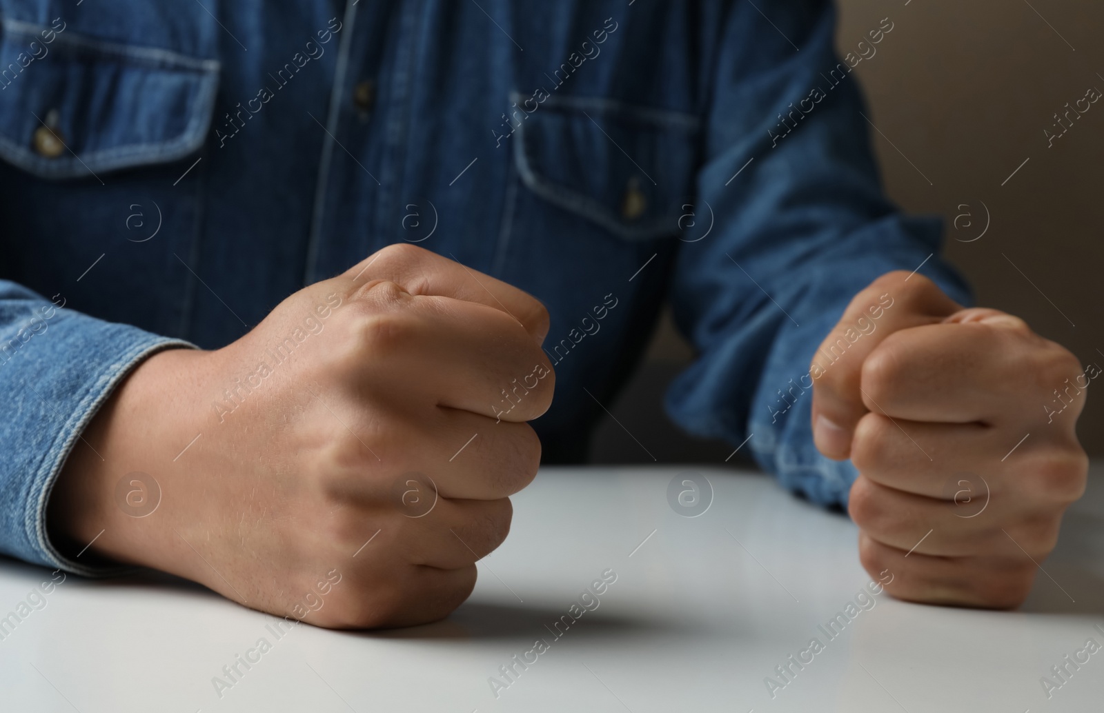 Photo of Man clenching fists at table while restraining anger, closeup