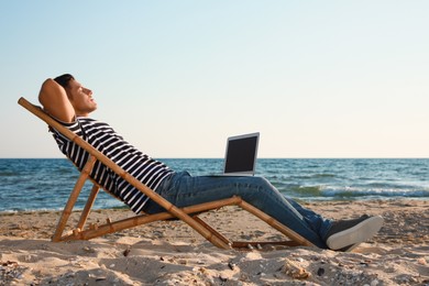 Photo of Man with laptop relaxing in deck chair on beach