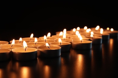 Wax candles burning on table in darkness, closeup