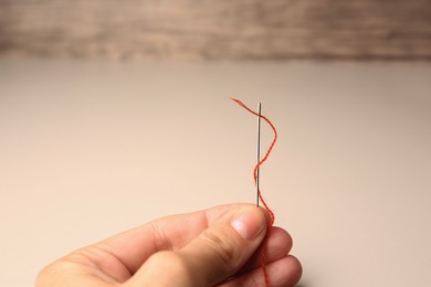 Woman holding sewing needle with thread at beige table, closeup. Space for text