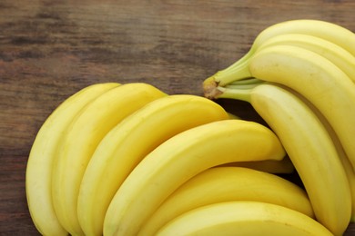 Photo of Bunches of ripe yellow bananas on wooden table, closeup