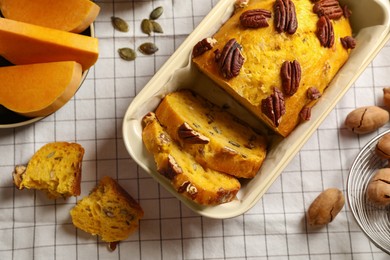 Photo of Delicious pumpkin bread with pecan nuts on tablecloth, flat lay