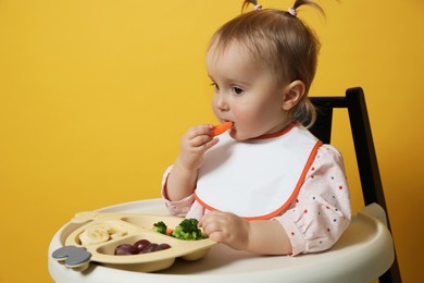 Photo of Cute little baby wearing bib while eating on yellow background