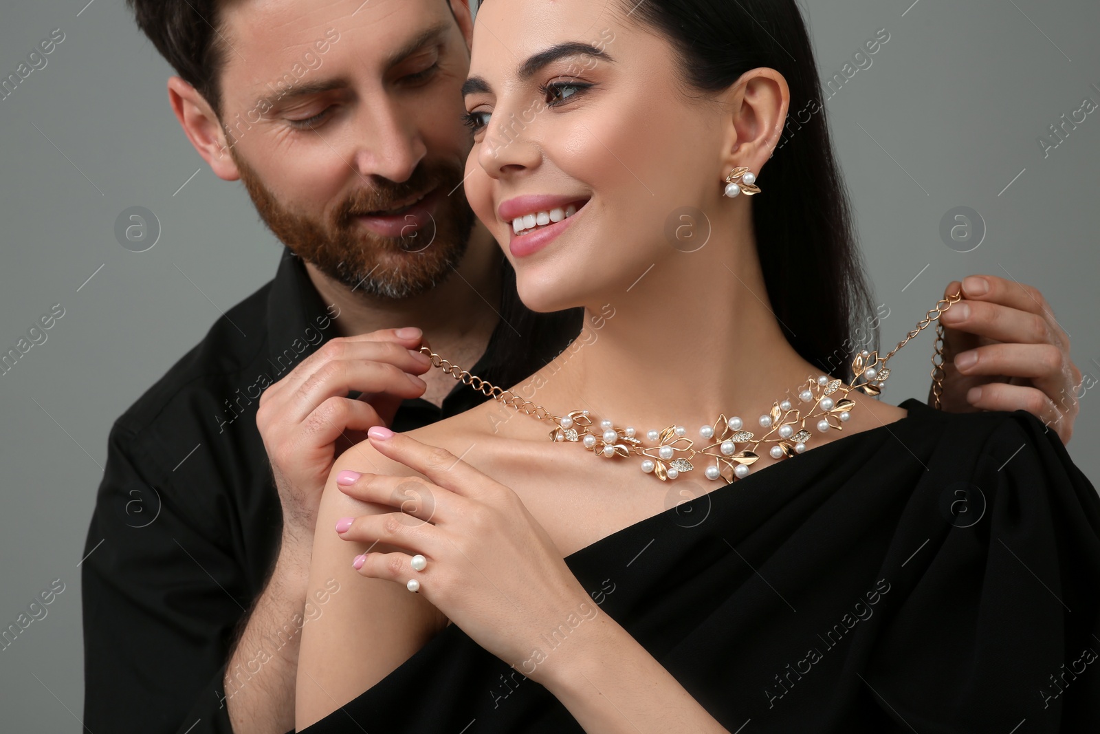 Photo of Man putting elegant necklace on beautiful woman against grey background, closeup