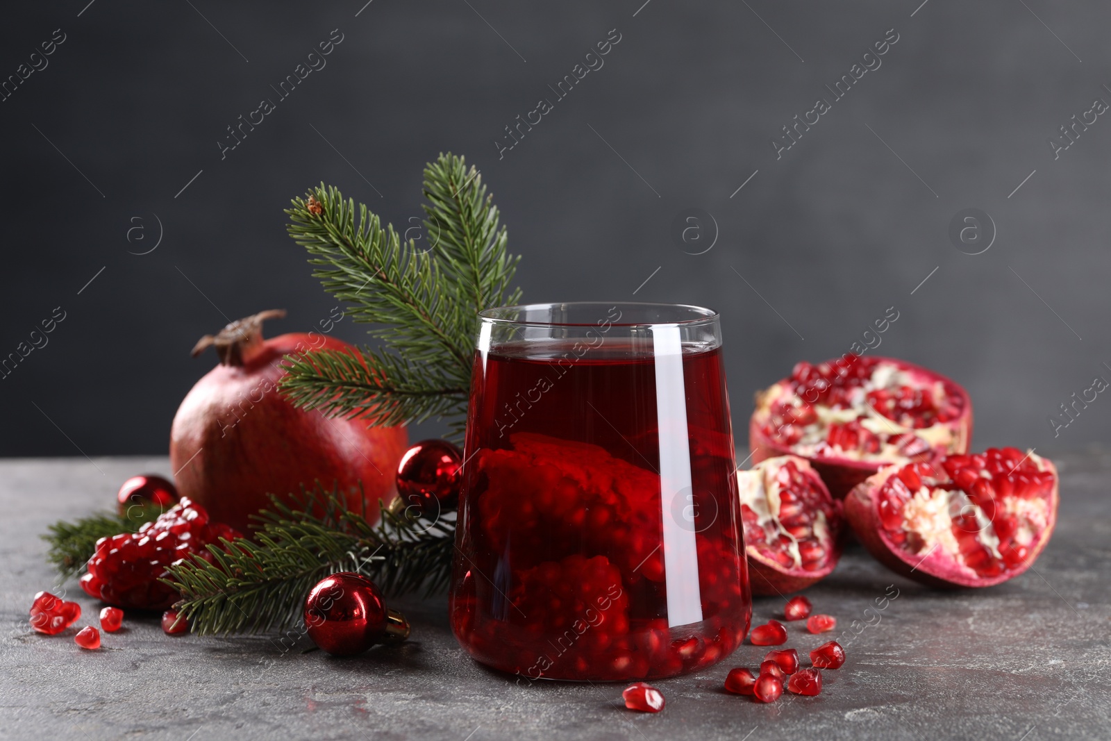 Photo of Aromatic Sangria drink in glass, Christmas decor and pomegranates on grey textured table