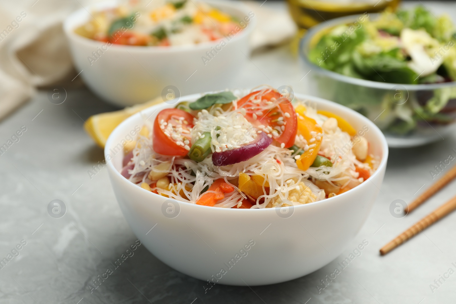 Photo of Tasty cooked rice noodles with vegetables on grey marble table