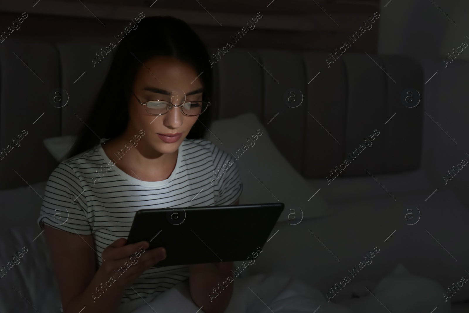 Photo of Young woman using tablet in dark bedroom