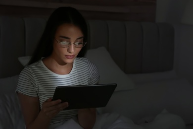 Photo of Young woman using tablet in dark bedroom