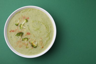 Photo of Delicious broccoli cream soup on green background, top view. Space for text