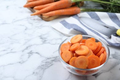 Photo of Slices of ripe carrots in glass bowl on white marble table, closeup. Space for text
