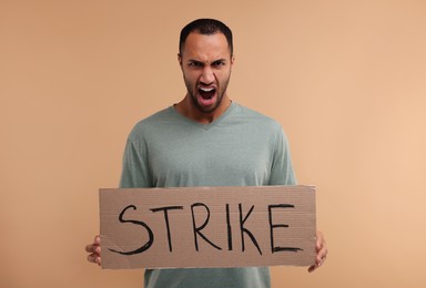 Photo of Angry man holding cardboard banner with word Strike on beige background
