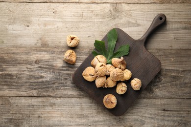 Board with tasty dried figs and green leaf on wooden table, flat lay. Space for text
