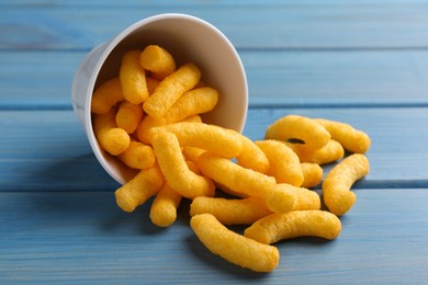 Photo of Many tasty cheesy corn puffs on blue wooden table