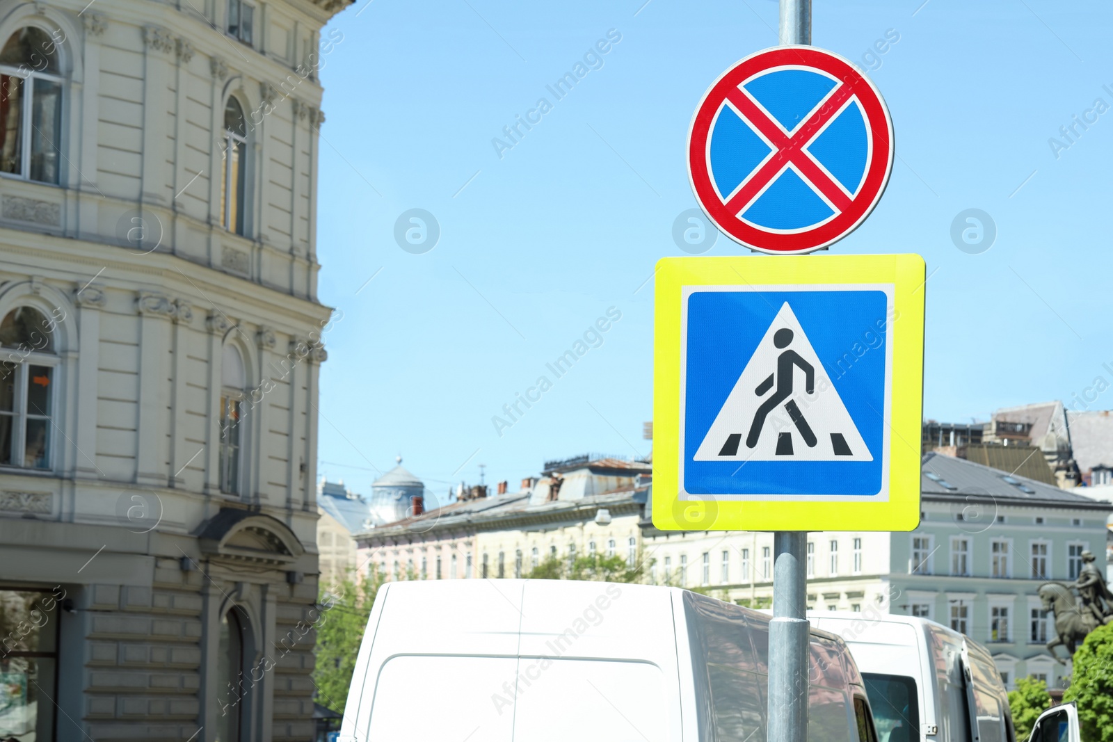 Photo of Post with Pedestrian Crossing and No Stopping traffic signs in city on sunny day