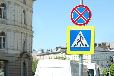 Post with Pedestrian Crossing and No Stopping traffic signs in city on sunny day