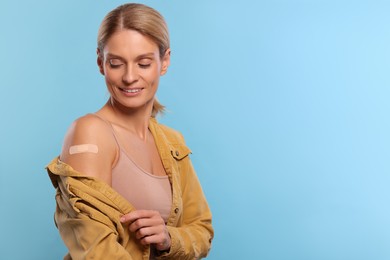 Photo of Smiling woman with adhesive bandage on arm after vaccination on light blue background. Space for text