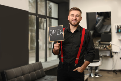 Photo of Young business owner holding OPEN sign in his barber shop