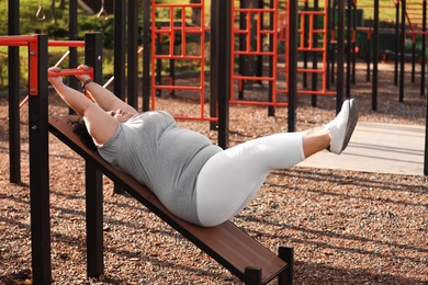 Photo of Beautiful overweight woman doing abs exercises on sports ground