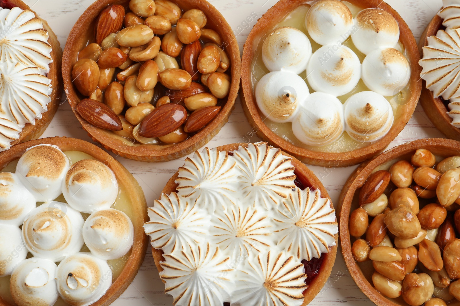 Photo of Many different tartlets on white wooden table, flat lay. Delicious dessert