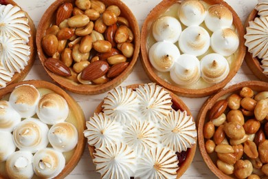 Many different tartlets on white wooden table, flat lay. Delicious dessert