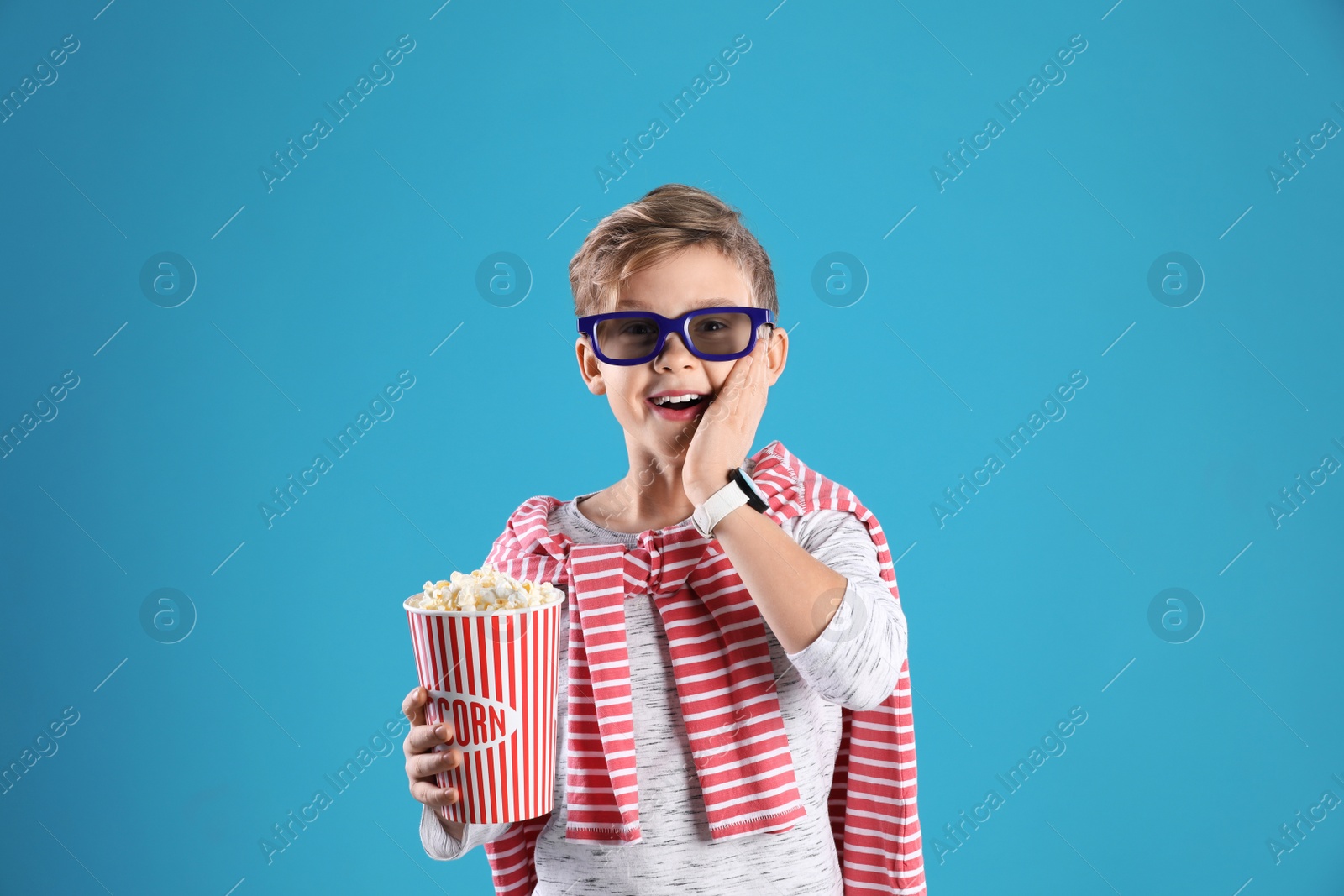 Photo of Cute boy in 3D glasses with popcorn bucket on color background